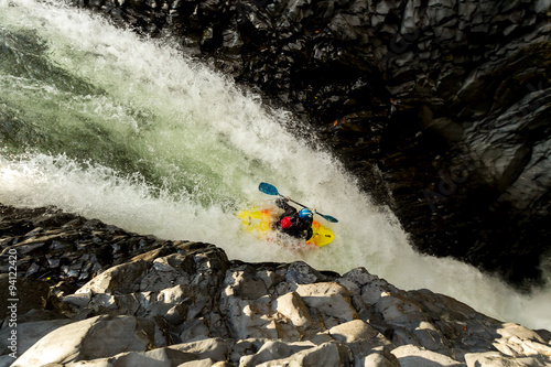 A bold man kayaks through white rapids, navigating a waterfall on a daring and extreme river rafting adventure.