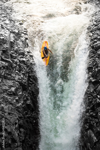 A thrilling image of kayakers navigating through dangerous white water rapids near a stunning waterfall, showcasing their courage and love for extreme sports.