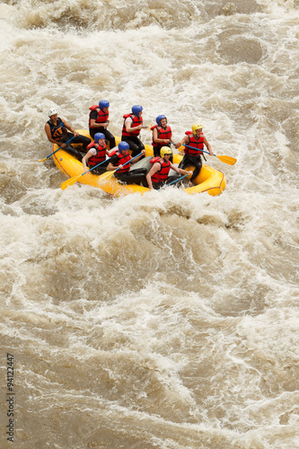 An assorted group of male and female travelers accompanied by an expert guide navigating turbulent river rapids during a whitewater rafting expedition in Ecuador