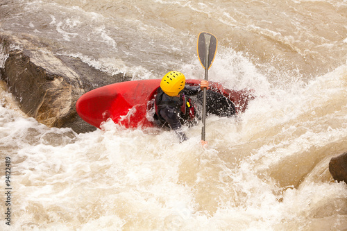 A group of adventurous individuals navigating through turbulent whitewater rapids in a kayak, with the stunning backdrop of a cascading waterfall.