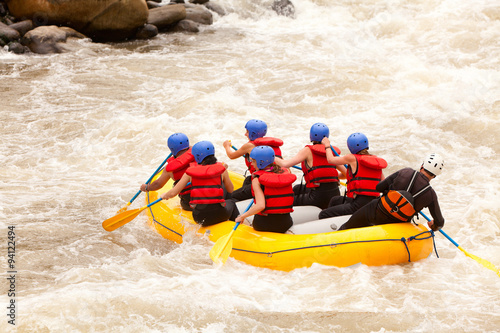 A group of people in a white water raft navigating through the rapids of a fast-flowing river.