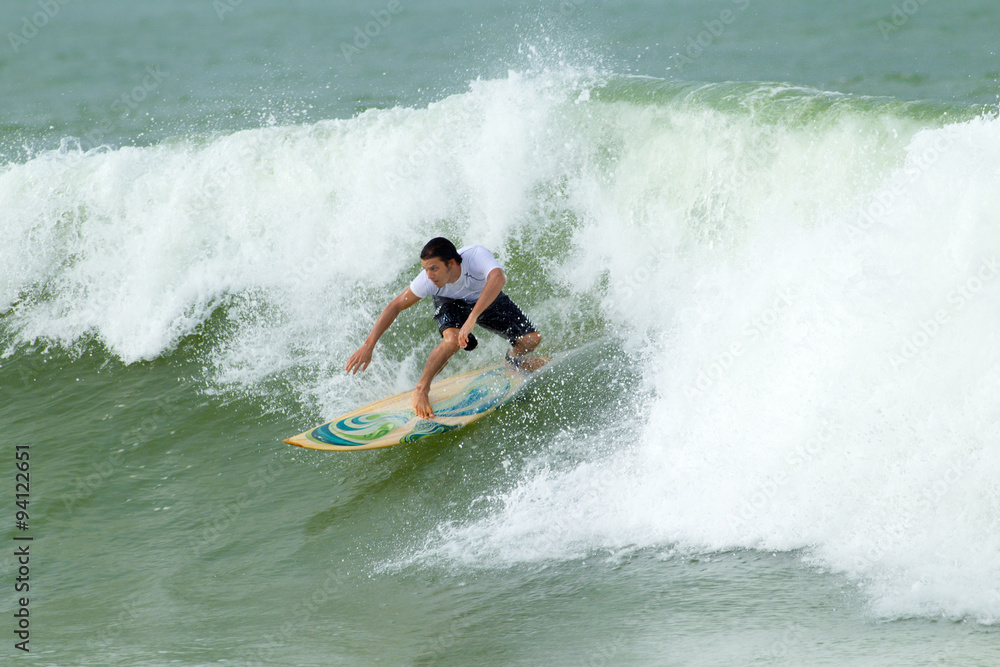 A man with a surfboard riding a massive wave, skillfully maneuvering through the water with the sun shining down on him.