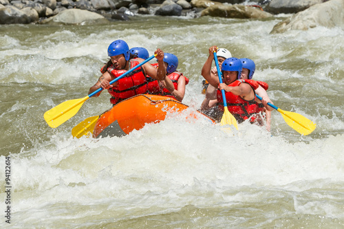 A team of extreme sports enthusiasts navigating through turbulent whitewater rapids on a raft, surrounded by the rushing white river water.