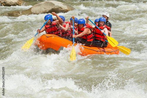 A team of people in helmets and life jackets navigate the white waters of a river while rafting, enjoying an adrenaline-filled sport.