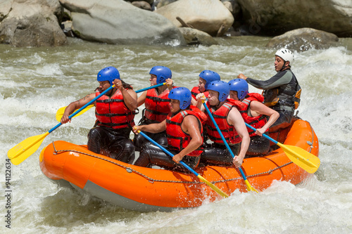 A team of adventurers in orange and yellow gear navigate a white water raft down a rushing river.