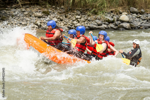 A group of friends wearing red life jackets navigating through white water rapids on a rafting adventure, laughing and having fun as a team.