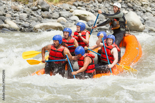 A team of people in a white water raft navigating through thrilling rapids on a fast-flowing river, having fun and enjoying the adventure.