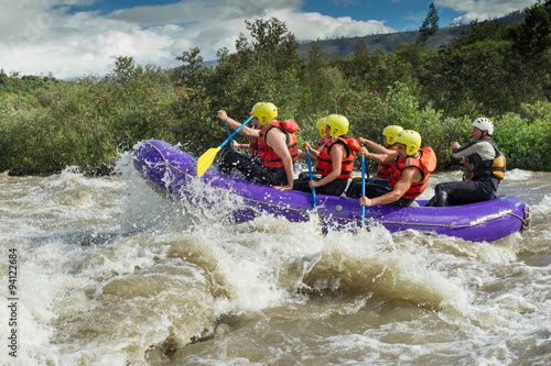 A team of men and women wearing helmets conquer the thrilling white rapids of an Ecuadorian river, united in their adventurous rafting competition.