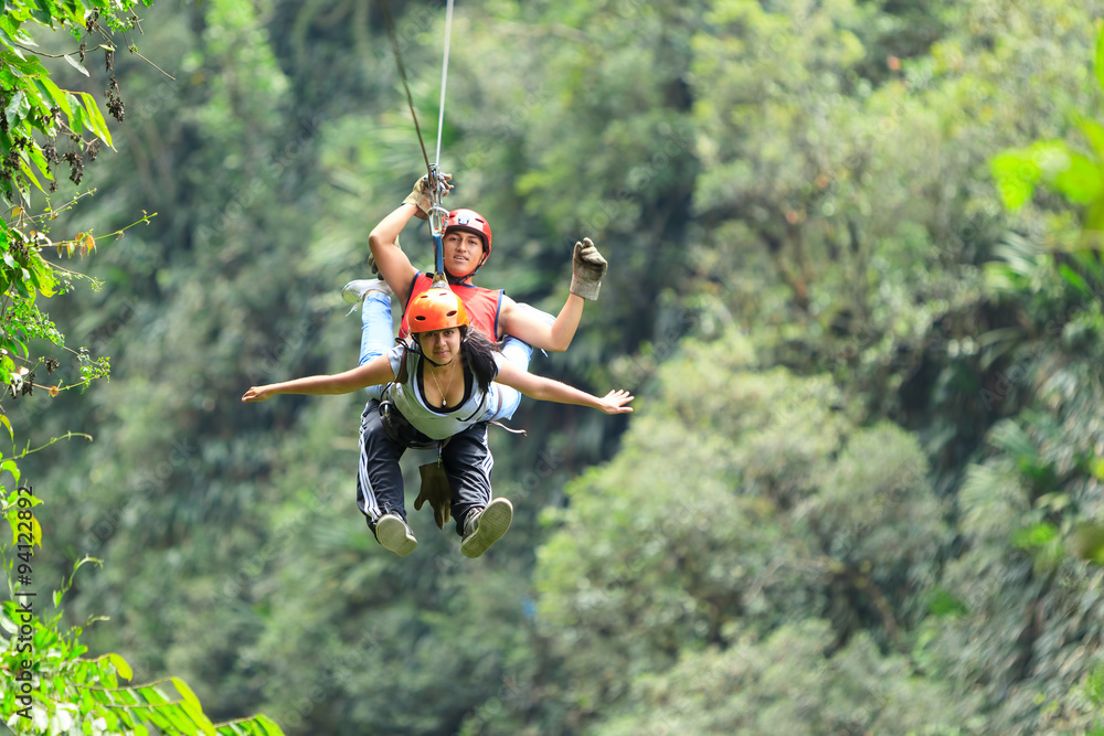 A couple on an adventure in the jungle of America, gliding through the canopy on a zip line, hanging from a wire as they travel. A couple on an adventure in the jungle of America, gliding through the canopy on a zip line, hanging from a wire as they travel.