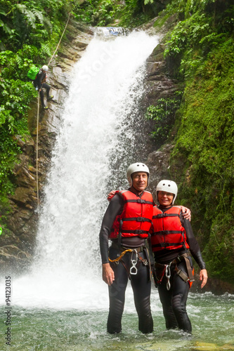 An elderly couple holding hands and smiling, ziplining through a canyon on their adventurous trip, showcasing their love for each other.