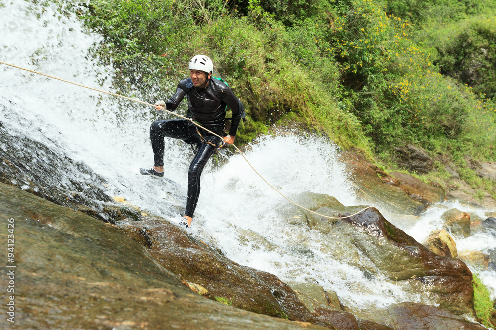 A daring canyoning enthusiast rappels down a dangerous waterfall surrounded by rocks, engaging in extreme water sport activities.