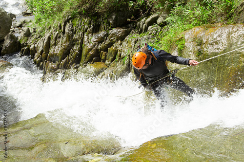 A daring adventurer rappelling down a waterfall in an Ecuadorian canyon, showcasing courage and skill in the thrilling sport of canyoning.