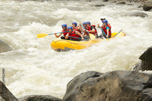 A woman in a white raft navigates challenging whitewater rapids in Ecuador, working as a team to conquer the intense water action.