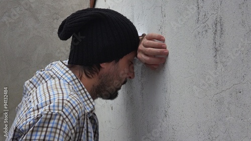 Troubled adult caucasian male banging his head against the wall, man with problems alone on the street.