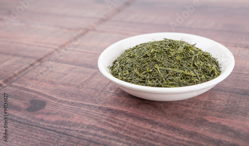 Dried green tea leaves in white bowl over wooden background