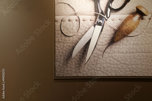 Art photo of scissors, leather and thread in photo frame on wall