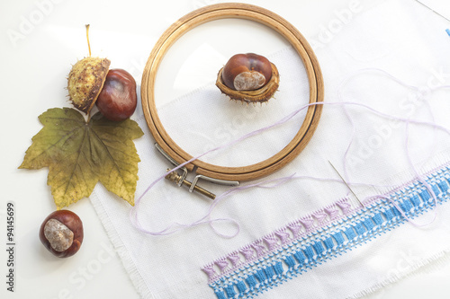 Mature chestnuts, autumn leaves and needlework on white background