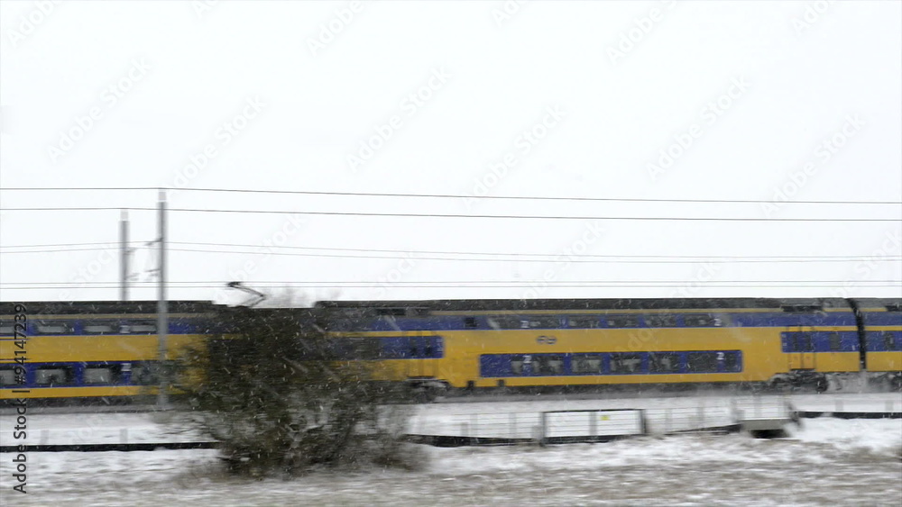 Dutch NS passenger train driving through a snowy winter landscape on a cold winter day. Dutch NS passenger train driving through a snowy winter landscape on a cold winter day.