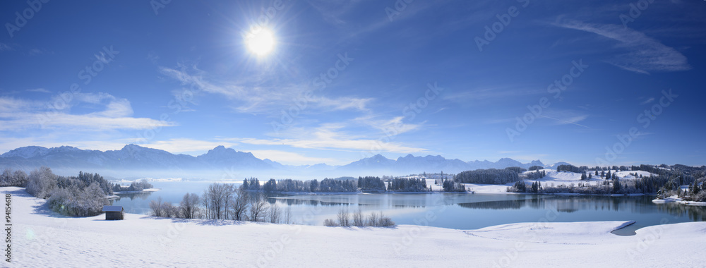 Fototapeta premium Panorama Winterlandschaft in Bayern im Allgäu mit Blick auf die Berge der Alpen und dem Forggensee bei Füssen