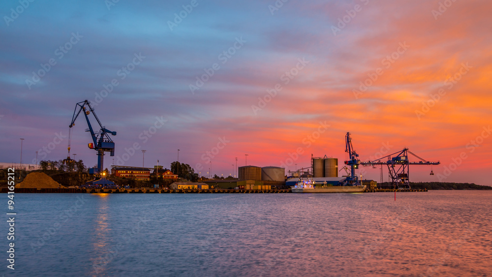 Massive blue cranes unload cargo in a seaport during sunset