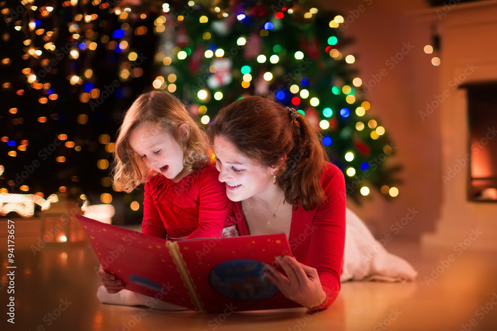 Mother and daughter reading at fire place on Christmas eve Mother and daughter reading at fire place on Christmas eve