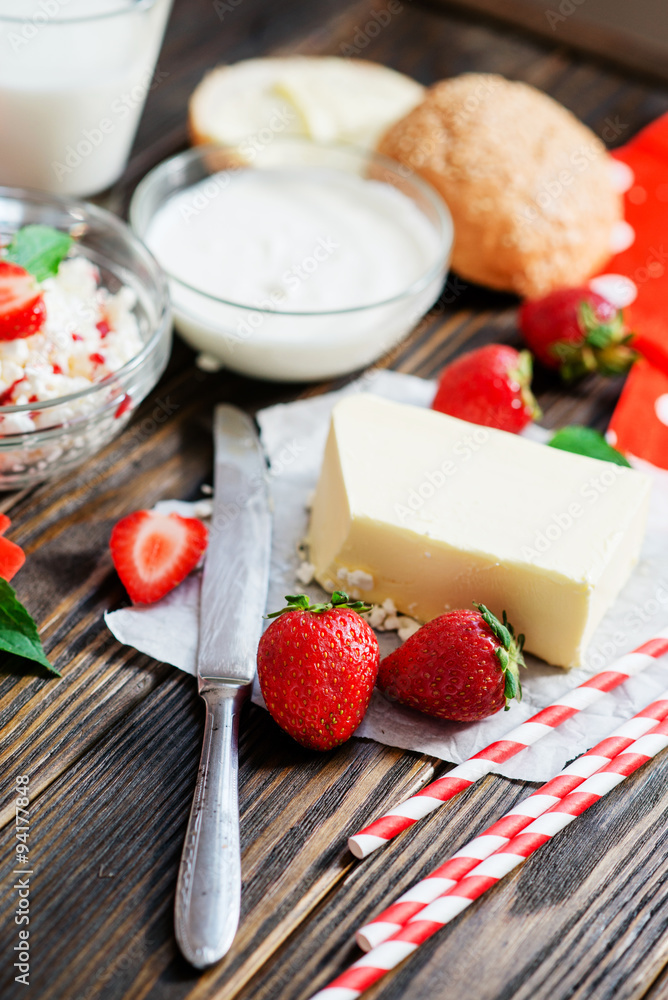 healthy breakfast of fruit and dairy products , cottage cheese with sour cream and milk, butter and roll , strawberries and syrup on a wooden background