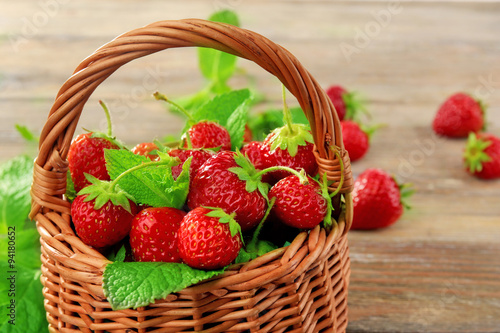 Ripe strawberries in wicker basket on wooden table, closeup