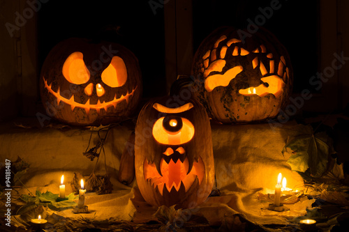 Photo composition from three pumpkins on Halloween. Jack, terrible hands, and a Cyclops of pumpkin against an old window, leaves and candles.