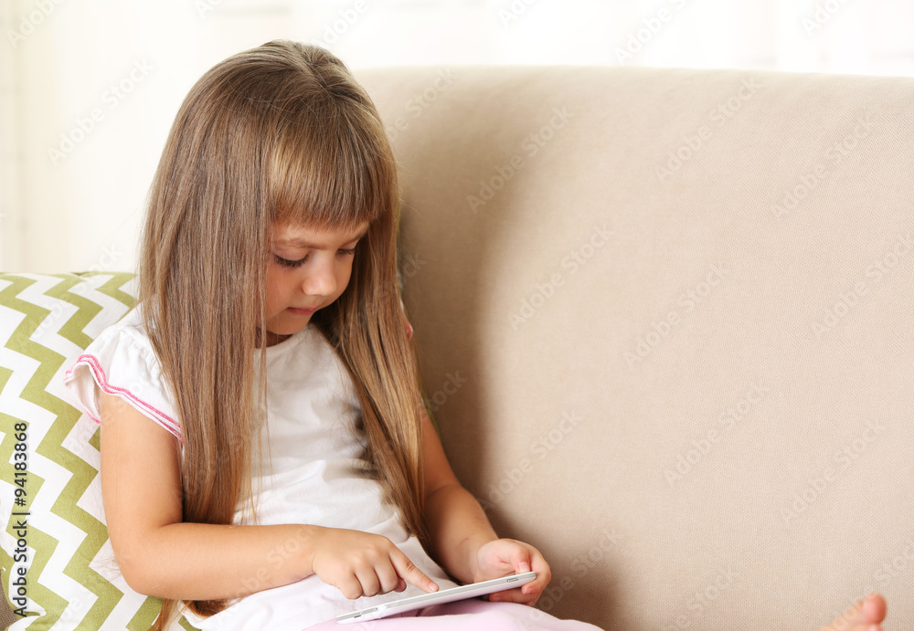 Beautiful little girl with smart phone sitting on sofa, on home interior background Beautiful little girl with smart phone sitting on sofa, on home interior background