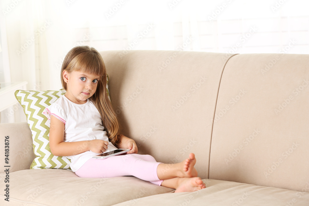 Beautiful little girl with smart phone sitting on sofa, on home interior background Beautiful little girl with smart phone sitting on sofa, on home interior background