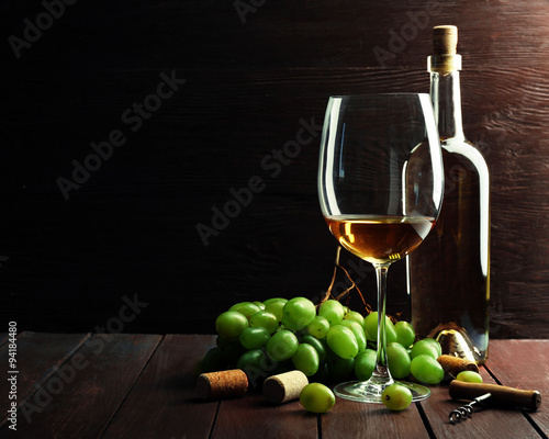 Bottle and glass of wine with grape on wooden background