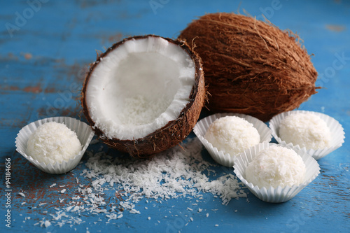 Candies in coconut flakes and fresh coconut on color wooden background