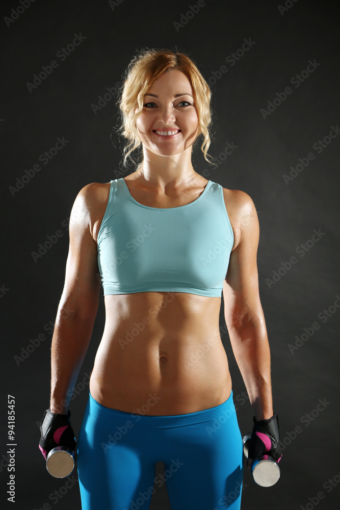 Athletic woman with dumbbells on dark background