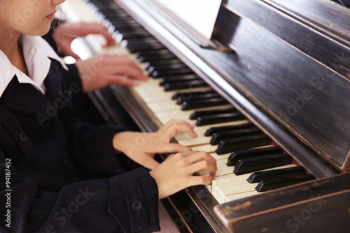 Musician teacher trains to play piano little girl, close up