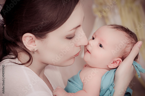 Mother kissing newborn baby on the background of crib