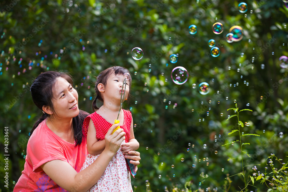 Asian lovely girl and her mother blowing soap bubbles. Family 