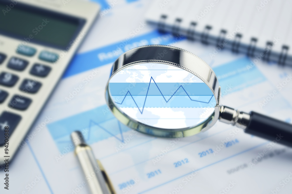 Magnifying glass, calculator and pen on financial graph Magnifying glass, calculator and pen on financial graph