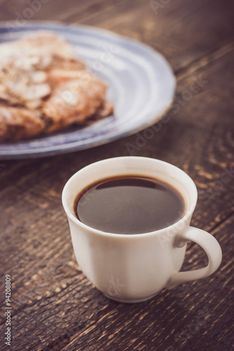 Cup of coffee with blurred croissant on the blue ceramic plate vertical