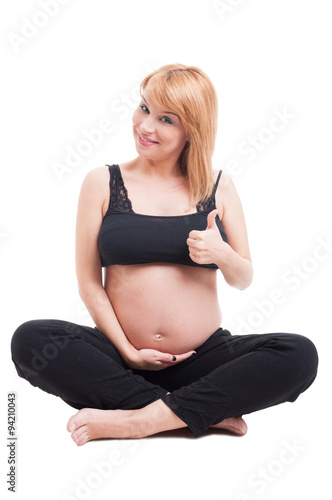 Happy pregnant woman sitting on white floor and showing like