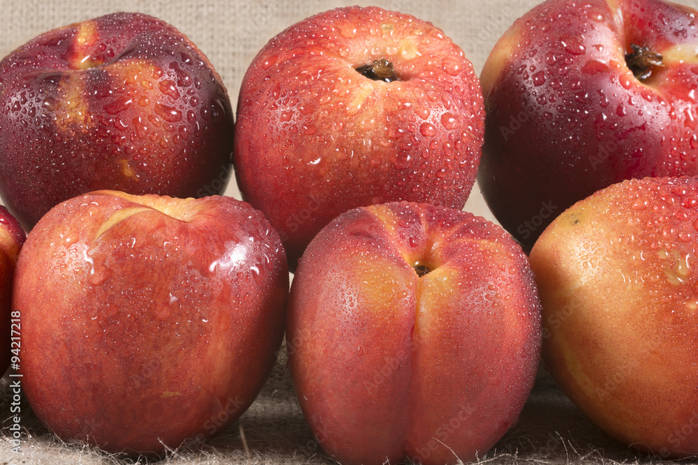 Ripe red peaches with drops of water on a burlap canvas close up Ripe red peaches with drops of water on a burlap canvas close up