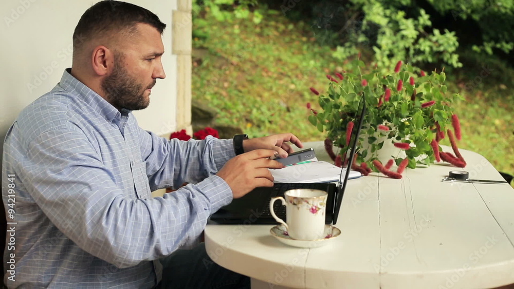 Man with laptop smoking cigarette on country house porch
Man with laptop smoking cigarette on country house porch