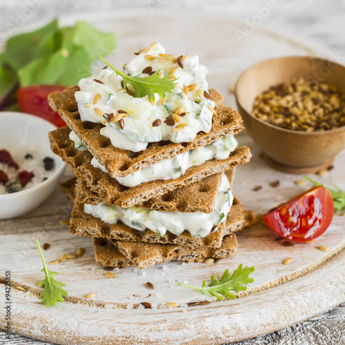 rye biscuit with cheese, cucumber and cilantro on a light wooden background - healthy snack