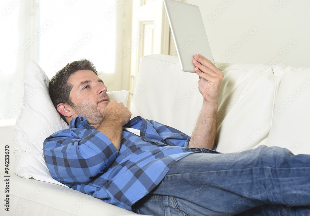 young attractive 30s man using digital tablet pad lying on couch at home networking looking relaxed