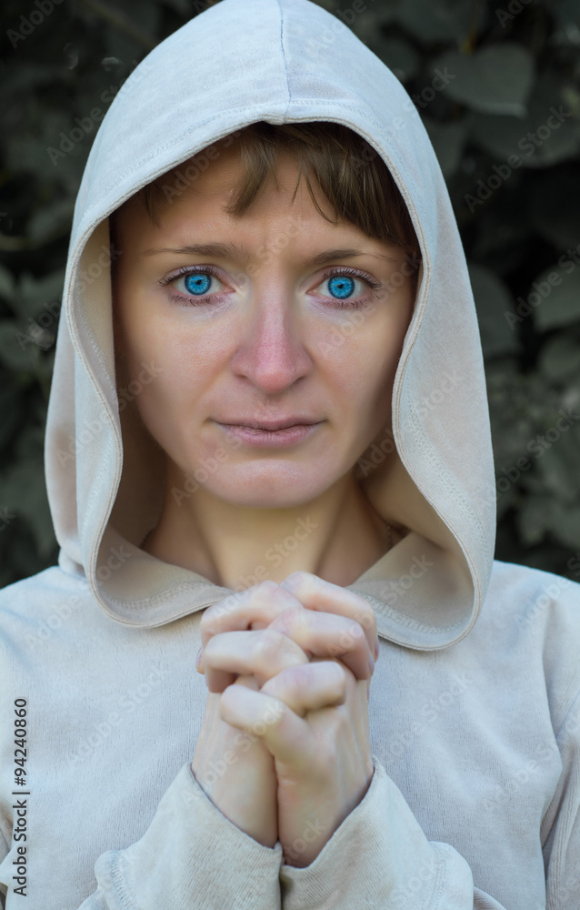 Obraz premium A girl wearing a jacket with a hood, put out his arms and folded her fingers together. As in prayer. 