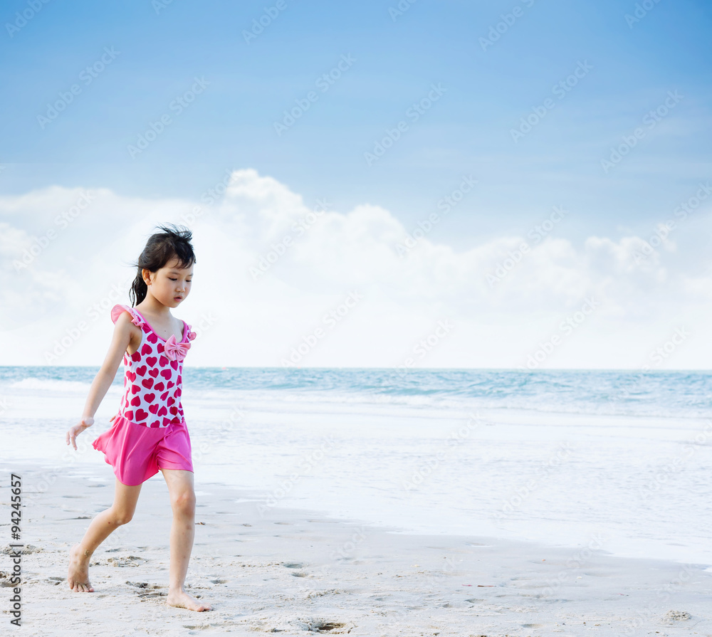 Young Asian girl in pink swim suit walk on the white sand beach