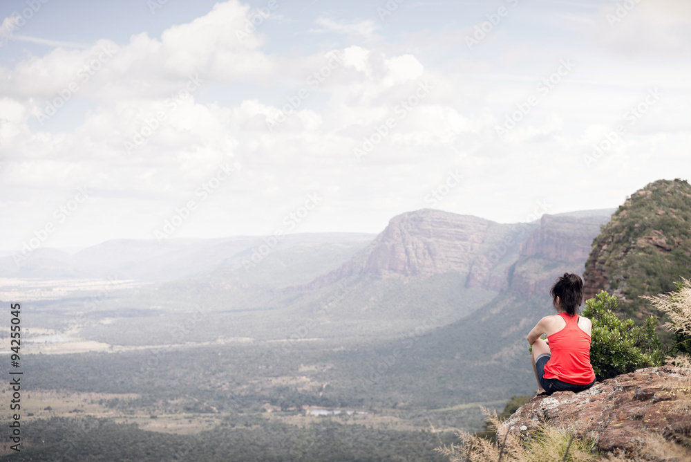 Young woman sitting at edge of cliff looking over expansive view