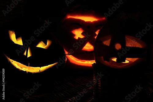 Three smiling Jack-O-Lanterns placed in darkness on wickerwork baskets. 