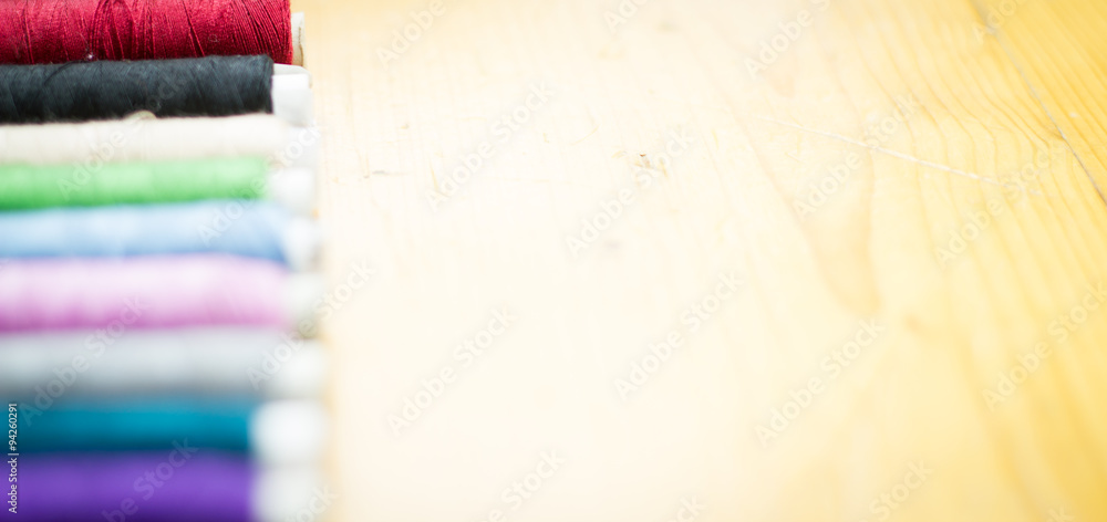 Fototapeta premium Bobbins with colorful threads on the wooden floor background / t