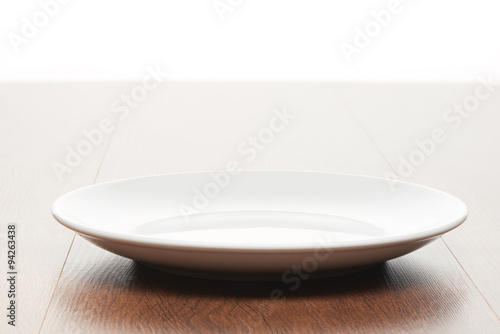 Empty white ceramic plate on bright light brown wooden table background
