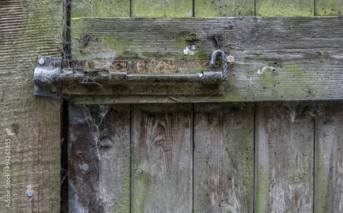 A very old, rusty door bolt , on an old, wooden door